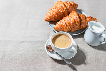 Croissants and cup of coffee in the morning light, sunlight shadow, on a linen fabric. Morning breakfast concept.