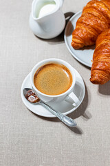 Croissants and cup of coffee in the morning light, sunlight shadow, on a linen fabric. Morning breakfast concept.