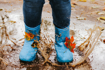 Teenager girl wearing blue rain boots jumping into a puddle on rainy autumn day. Closeup.