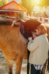 Keen ginger girl preparing her horse for the ride, attaching saddle, fastening