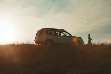 Fototapeta premium woman silhouette near suv car on sunset