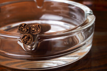 Three cigars in a round glass ashtray, close-up, shallow depth of field.