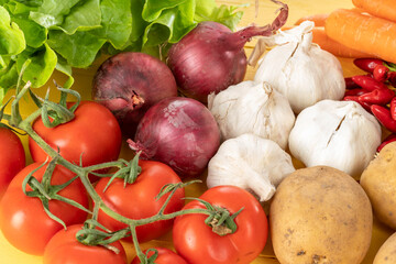 Tomatoes onions garlic green salad and potatoes on a yellow wood background