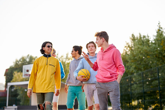 energetic, healthy teens have fun, talk before playing basketball, group of happy teenage boys in colourful casual wear, playing basketball outdoors in the city, go at playground