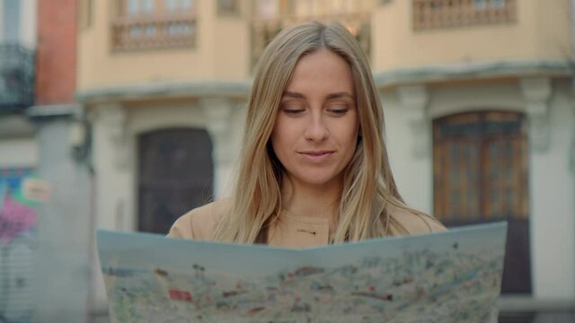 Portrait of beautiful authentic young woman with blonde hair and blue eyes, look direct into camera and smile. Excited and amazed, explore new place with map. Travel wanderlust concept
