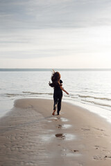 Young beautiful girl in black clothes walking on the beach. She walks along shore. A walk at sunset. Nobody around. Laugh, smile and enjoy summer Vacations. Footprints in the wet sand