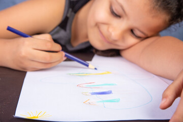 Small Brazilian girl drawing with colored pencils, lying on the drawing, selective focus.