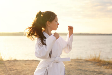 Cute little girl in kimono practicing karate near river on sunny day © New Africa
