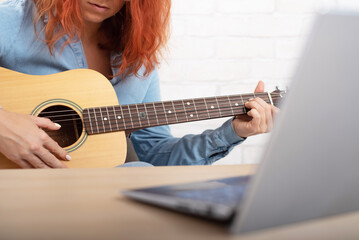 Young woman learns to play the guitar by video on a laptop. Online music lessons