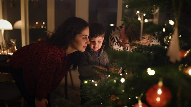 Christmas holidays. A boy looking at the lights on the Christmas tree together with his parents. Interior shot of a family home decorated for Christmas.
