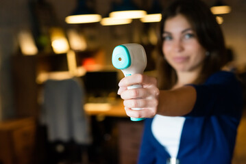 Beautiful smiling woman measures body temperature with infrared thermometer in the office