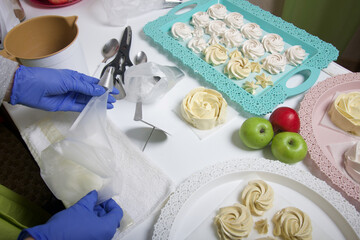 A woman in rubber gloves and a medical mask makes homemade marshmallows. Fresh marshmallows are nearby on a tray. Cooking sweets during a pandemic.