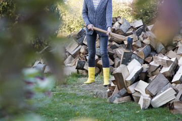 Woman in yellow rubber boots chopping woods with axe. Homestead chores for the fall on farm.