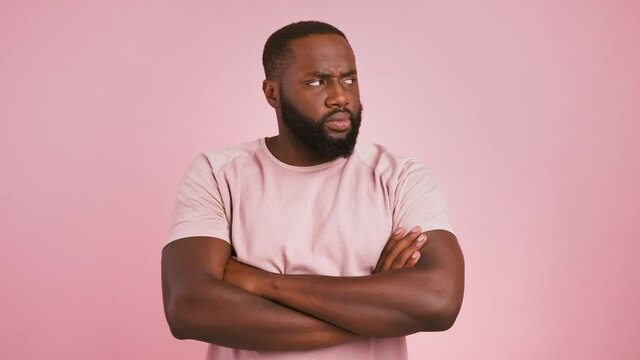 Offended african american guy folding arms and pouting lips to camera, pink background