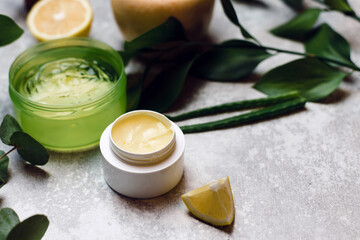 Yellow natural moisturizer in a white jar on a gray background. Cream of natural ingredients, aloe, eucalyptus, lemon and leaves. Perfect homemade natural face mask