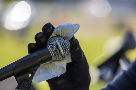Selective focus of hands of unrecognized person wearing black safety gloves while cleaning mic with napkin before speaking over it