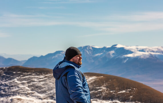 View of a tourist looking in the distance in the mountains. White snowy mountain ridge and beautiful blue cloudy sky as a background and slightly out of focus. Altai mountains, Siberia, Russia
