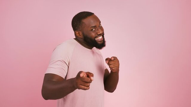 Profile portrait of black man turning to camera and indicating happily at camera, choosing, pink studio background