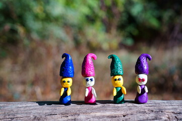 Figures of four fairy-tale dwarfs made of plasticine in the forest on a colored background.