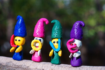 Figures of four fairy-tale dwarfs made of plasticine in the forest on a colored background. The elves have letters in their hands. The inscription love.