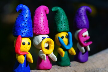 Figures of four fairy-tale dwarfs made of plasticine in the forest on a colored background. The elves have letters in their hands. The inscription love.