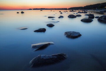 Fototapeta na wymiar Stones on sea coast. Sunset over the sea. Deep blue color of summer late sunset. Long exposure