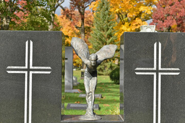 A bronze figure on a monument in a cemetery as autumn displays color in the background.