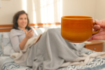 Obraz na płótnie Canvas Image with focus on cup and defocused young woman reading in background