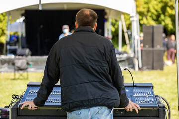 Rear view of young man wearing jacket standing behind electronic sound equalizer while staring at...
