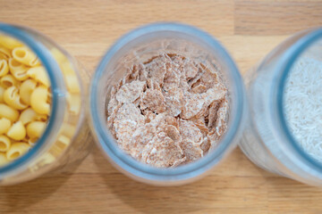 Glass jars with  flakes, rice and pasta on wooden table top view close up. Storing bulk food at home