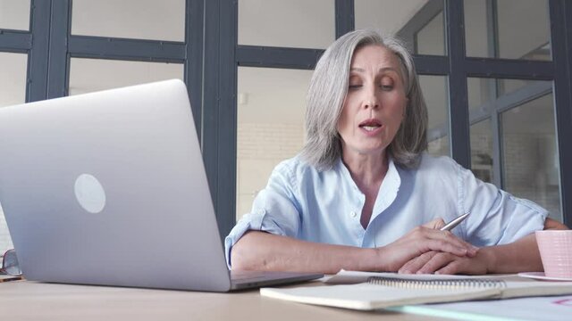 Middle aged business woman talking video conference calling on laptop. Senior old distance teacher communicating in online virtual chat remote meeting looking at computer working from home office.