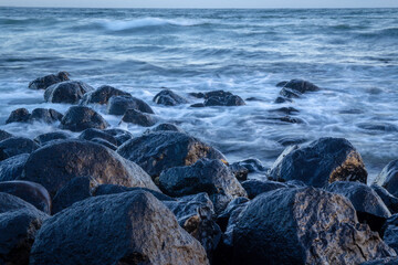 Fototapeta na wymiar Waves washing over rocks in slow-motion, early morning sunrise. Blue, green and turquoise sea colors. Burleigh Beach, Gold Coast, Australia. 
