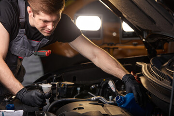 young caucasian professional auto mechanic in a car service, checks a car, engine, carburetor. car...