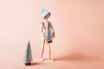 Wooden mannequin in red Santa hat is carrying tiny christmas tree, concept of preparation for Xmas holidays, going home for festive time concept
