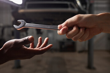 two young diverse mechanics hands giving, sharing tool to each other. automotive craftsman during...