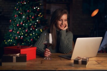 Woman drinking wine, using laptop, shopping online. Christmas tree in the background.