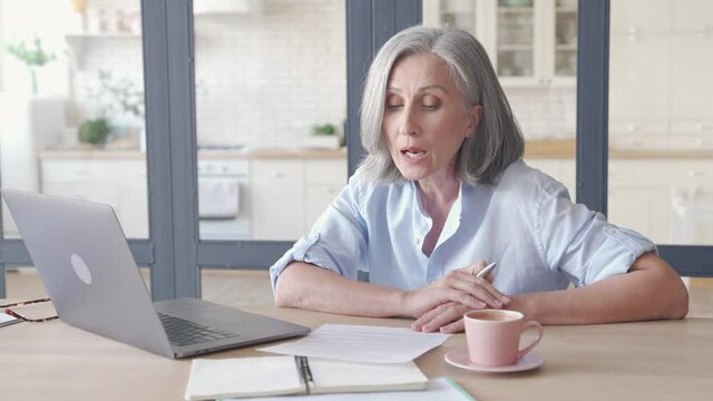 Mature older senior business woman distance teacher, coach, tutor, talking giving web training, live webinar making video conference call virtual chat meeting on laptop working from home or in office.