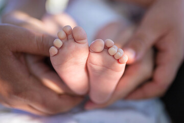 Newborn baby girl feet in parents’ hands outside