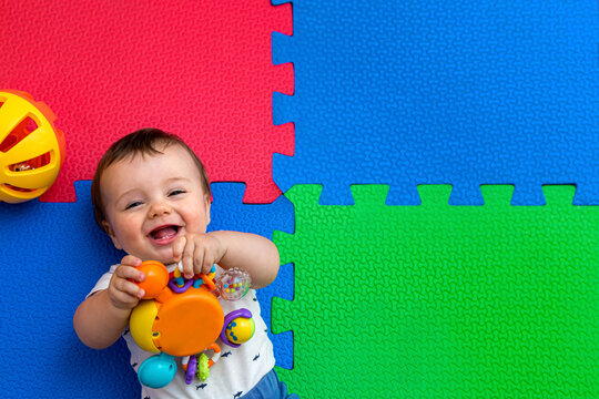 Funny baby playing on colorful eva rubber floor. Toddler having fun indoor his home. Top view. Copy space.