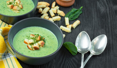 Spinach cream soup with crackers, herbs on a dark table. Green soup is served in a bowl on a wooden table. Side view.