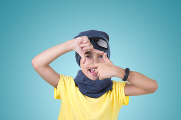 A child in a yellow t shirt hat and scarf is photographed on a light turquoise background