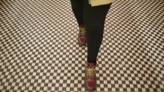 Feet in boots step on the checkered floor of the restaurant. Gait of a joyful person in motion. Take beautiful steps, the view from the top.