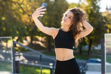 Selfie portrait young cheerful fit woman in sports top smiling outdoors in park