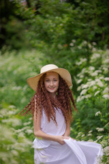 Cute red girl in straw hat on a flowering clearing at a picnic with fruit