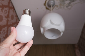 Female hand holding a led light bulb to change, replace it at home, screwing in the bulb into a lamp holder for energy saving and economy, saving money