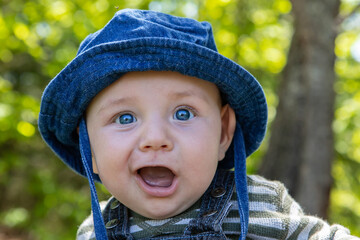 Portrait of cute little infant with blue eyes hat sitting in park with mouth wide open enjoying and relaxing outdoor garden 