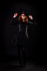Young woman in black dress and witch hat on a black background.