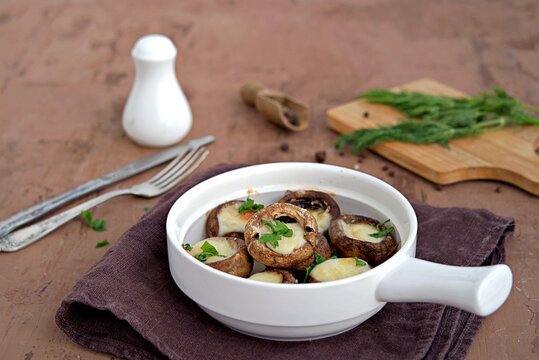 Hot appetizer, baked mushrooms with suluguni cheese in white ceramic form.