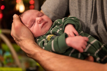 Selective focus of portrait of unwell cute little newborn baby sleeping and resting peacefully in the arms of father at home 