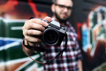 Hipster guy holding a retro photo camera close-up on his outstretched hand. Blurred background